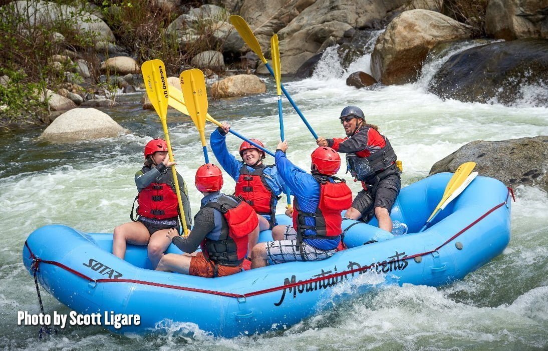Whitewater rafting guide demonstrated paddle handling as four adults in life preservers and helping prepare to take on a churning river