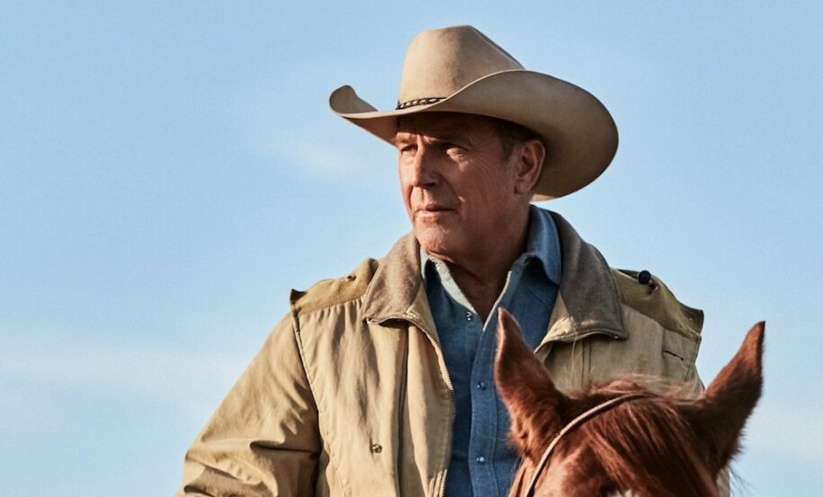Kevin Costner, wearing a cowboy hat and range jacket sits astride a reddish-brown horse.